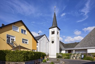 St Anthony's Church and residential building against blue sky with cirrus clouds in Beuren, Eifel,