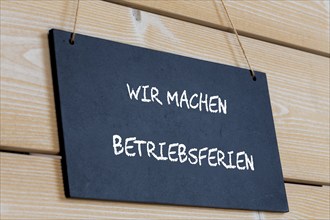 Symbolbild für Betriebsferien: Schild auf einer Holztafel mit der deutschen Aufschrift WIR MACHEN