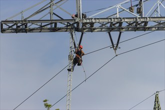 A technician works on a high-voltage pylon under a clear blue sky