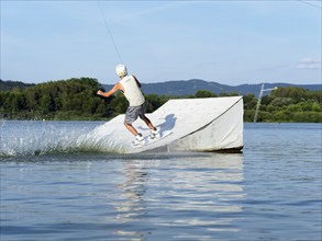 Sporty young man with wakeboard, jump over obstacle, jump, water sports, water skiing and wake