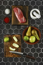 A variety of fresh ingredients lie on chopping wooden boards, including raw meat, vibrant apples