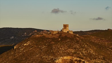 Wide view of an old castle in the mountains, illuminated by the last rays of the setting sun,