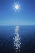 Midday sun over Mediterranean sea with small boat and landmass in the background, Rhodes, Greece,