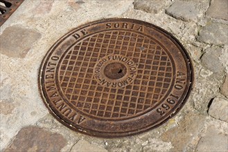 A round cast iron manhole cover with engraved text on cobblestones in a town, manhole cover,