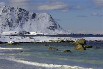 Snowy beach with rocky mountains in the background, gentle waves in the blue sea, calm winter