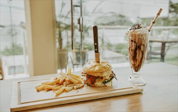 Hamburger with fries and milkshake served on wooden board with space for text