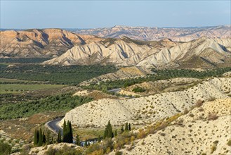 Wide desert landscape with rocky hills and serpentine road under a blue sky, Dehesas de Guadix,