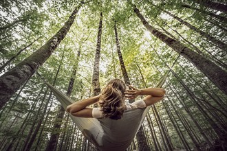 A woman lies in a hammock and looks up at the wooded sky