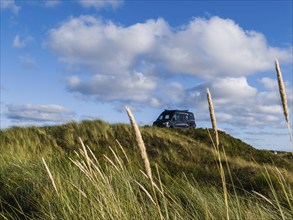 A campervan stands on a grassy dune under a blue sky with clouds, North Sea, Jutland, Denmark,