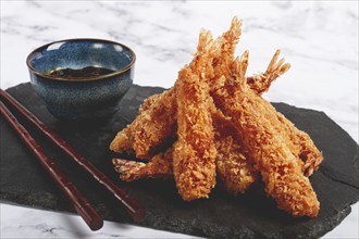 Shrimp in tempura, deep fried, on black slate, with sauce, light marble table, no people