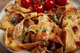 Pappardelle pasta with bolognese sauce, topped with parmesan cheese and cherry branch, homemade, no