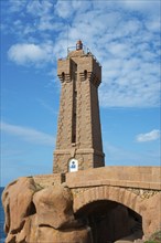 Lighthouse above an arch of rocks in front of a blue sky with clouds, Phare de Men Ruz,