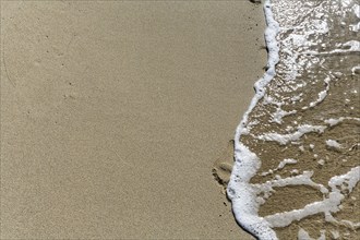 Gentle wave on the shore blurs footprint in the sand, Simos beach, text free space, symbolic photo,