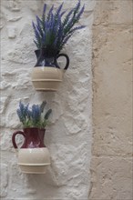 Jugs with artificial flowers hanging as decoration on a white house wall, Cisternino, southern