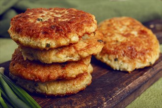 Crispy potato pancakes Latkes, stacked on a wooden board next to fresh green onions, natural light,