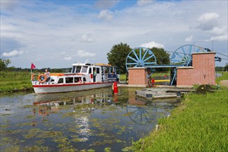 A boat passes a lock in a green landscape in sunny weather, ship Zefir, manoeuvrable wheels in the