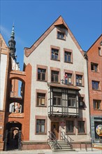 A historic half-timbered building with red brick elements and a high tower in the background under