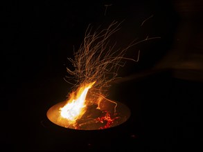 Garden Barbecue Pan, filled with burning wood, creating flames and sparks against the nighttime