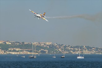 Stunt aerobatic plane Edge 540 performing stunts in blue sky at Oeiras Air Show above yacht boats