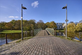 Pedestrian bridge Dankwartsbrücke, lanterns, trees, blue sky with fair weather clouds, river Trave,