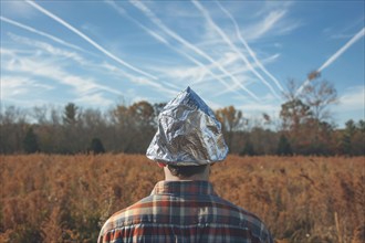 Chemtrail conspiracy theory concept with back view of man with tinfoil hat looking at sky with