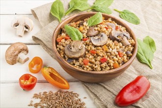 Spelt (dinkel wheat) porridge with vegetables and mushrooms in wooden bowl on a white wooden