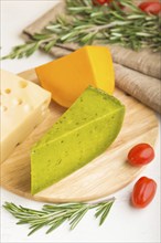 Green basil cheese and various types of cheese with rosemary and tomatoes on wooden board on a