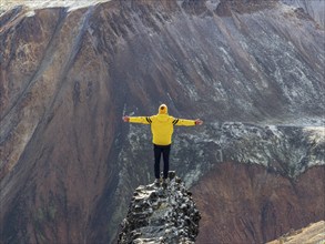 Tourist poses on a rock, early snow on the colorful rhyolite mountains, Landmannalaugar, Fjallabak