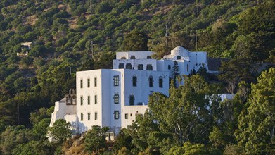 A white monastery with green windows, nestled in wooded hills under a clear sky, Monastery tis