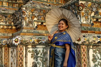 Traditionally dressed woman with umbrella poses in front of the temple Wat Arun or Temple of Dawn