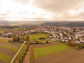 Aerial view of a town in autumnal surroundings with clouds and fields, Tiefenbronn, Germany, Europe