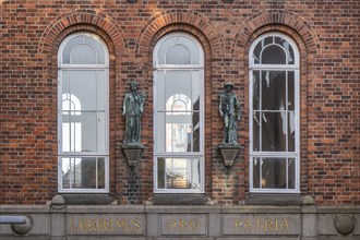 Facade of a brick building with Latin inscription and sculptures between windows, elephant tower,