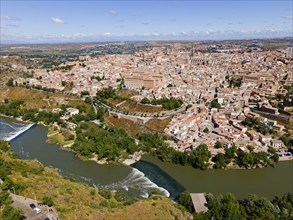 View of a historic city with a river surrounded by green vegetation under a slightly cloudy sky,