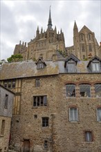 View of the Mont Saint-Michel buildings, dominated by towers and stone facades under a cloudy sky,