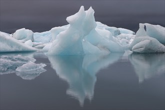 Symmetrical ice structures reflected in the calm water, grey sky, Jökulsárlón or Jökulsarlon