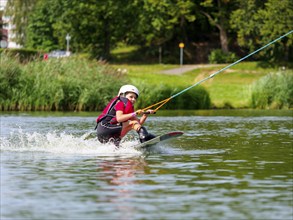 Boy or girl, water sports with wakeboard, red life jacket, water skiing in the wake park