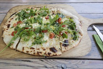 Original tarte flambée with bacon and rocket served on a wooden board in a garden restaurant,