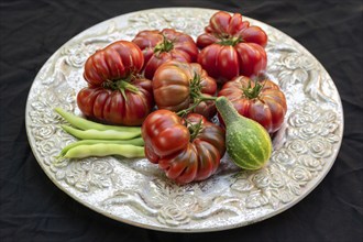 Tomatoes, ox hearts and a Vorgebirgstrauben pickled cucumber on a decorative plate on a black