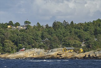 Coastal landscape with rocks, several houses and forest under a cloudy sky, Holiday homes,