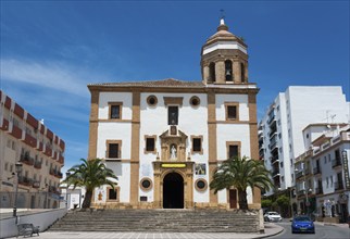 Large church with palm trees in the foreground, surrounded by urban buildings under a bright sky,