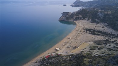 Aerial view of a secluded sandy beach landscape with clear blue water and a few huts, Tsambika