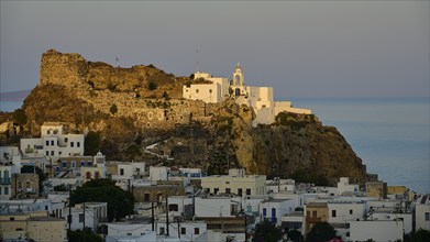 A historic castle and white houses on a hill overlooking the calm sea in the soft light of dawn,