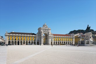 Spacious square with a large yellow building, arcades and a statue, all under a clear blue sky,