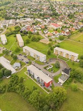 Bird's eye view of several buildings of a town surrounded by green fields and under a partly cloudy