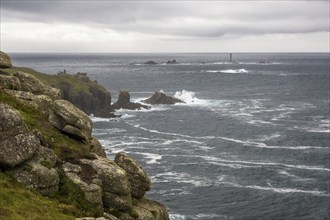 Rugged coastline with large rocks and a lighthouse in the distance, under a cloudy sky, Land's End,