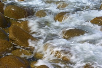 Water flows over brown stones surrounded by waves. Dynamic and natural atmosphere, Point du