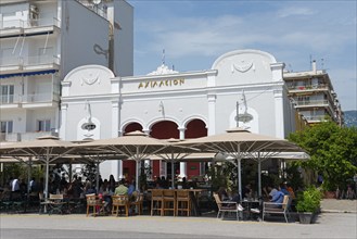 A white building with restaurant and terrace where people sit in sunny weather, cinema, Achilleion,