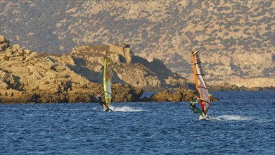 Two windsurfers in rough sea off rocky coast, windsurfer, Meltemi windsurfing spot, Devils Bay,