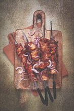 Pork kebab on skewers, with red onion, on a wooden chopping board, close-up, top view