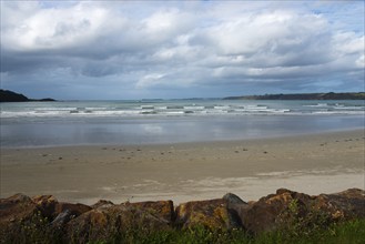 Lonely beach with gentle waves, covered by a cloudy sky and surrounded by rocks, Plage Saint